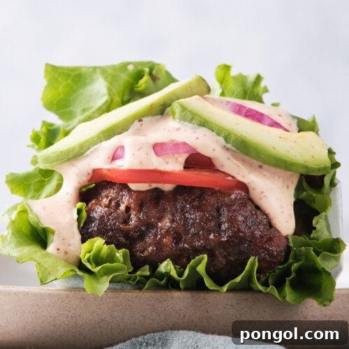 Side view of a Whole30 burger with spicy mayo wrapped in lettuce with tomatoes and red onion.