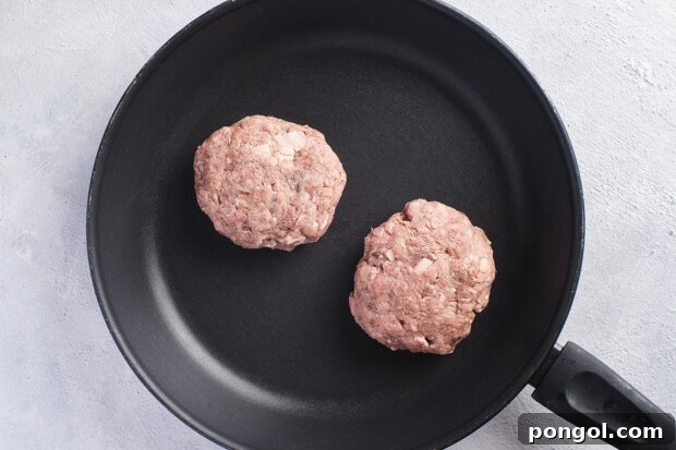 Overhead view of 2 Whole30 burger patties in a large cast iron skillet.
