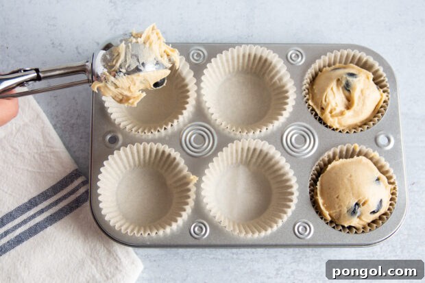 Overhead view of muffin batter added to muffin tin lined with parchment paper baking cups on counter top.
