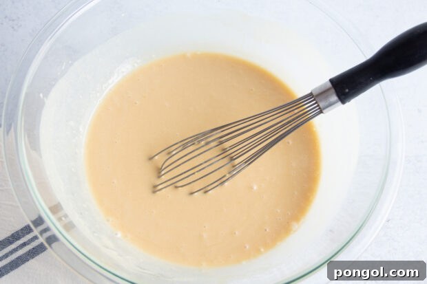 Wet ingredients for gluten free blueberry muffins in large glass mixing bowl with whisk.