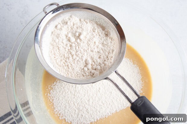 Dry ingredients for gluten free blueberry muffins in sifter over wet ingredients in large glass mixing bowl.