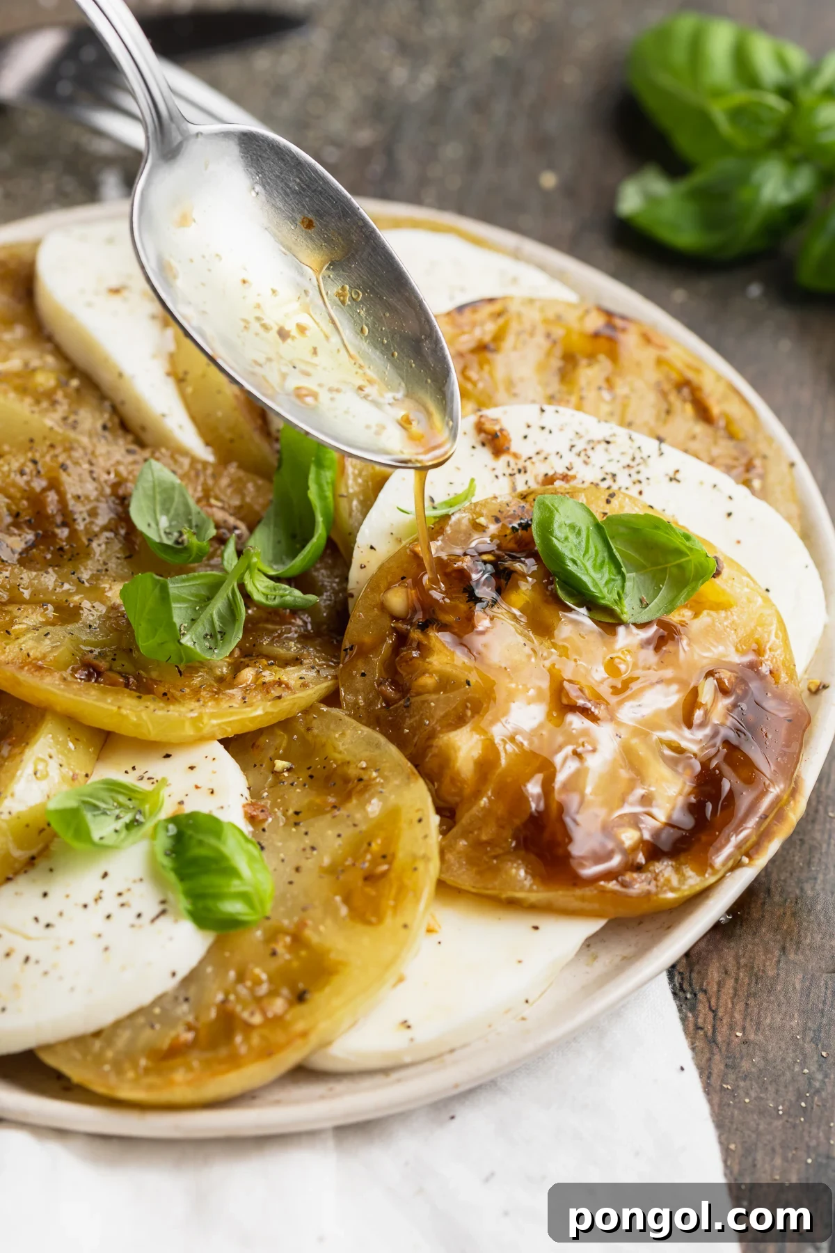 Balsamic vinaigrette being drizzled over perfectly grilled green tomatoes and slices of fresh mozzarella, artfully arranged on a platter with basil.