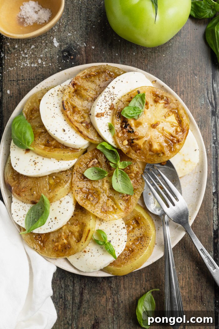 Overhead view of grilled green tomato slices alternating with mozzarella rounds on a plate with fresh basil, garnished.