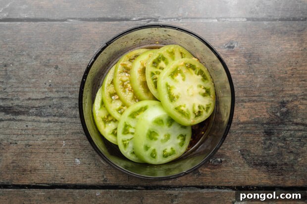 Green tomato slices immersed in a rich balsamic marinade within a large bowl.