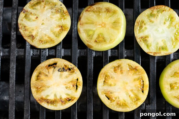 Sliced green tomatoes marinated in balsamic sauce arranged on a hot grill grate.