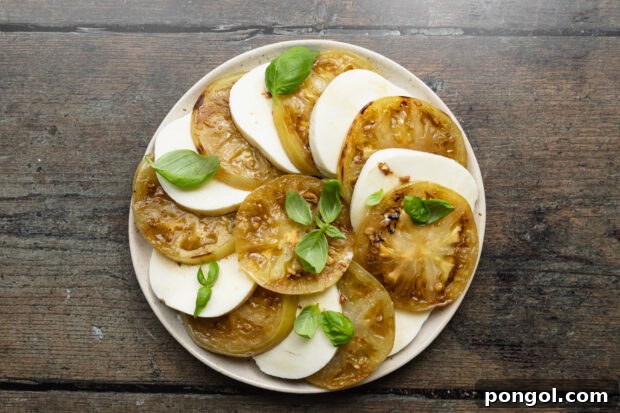 Overhead view of grilled green tomato slices alternating with mozzarella rounds on a plate with fresh basil, garnished.