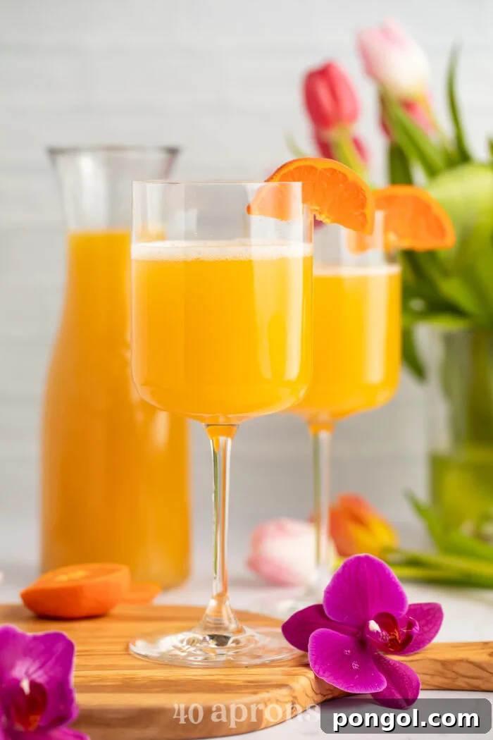 Side view of two wine glasses holding POG juice mimosas with a carafe of pog juice in the background.