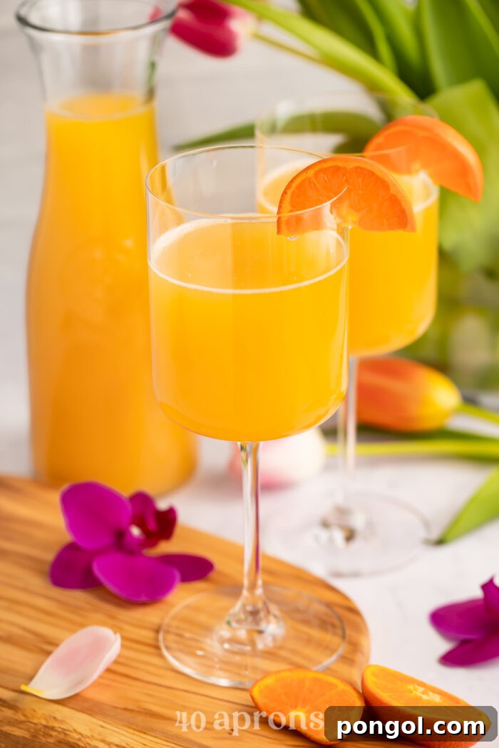 Overhead, angled view of POG juice mimosas in two wine glasses with a carafe of juice in the background.