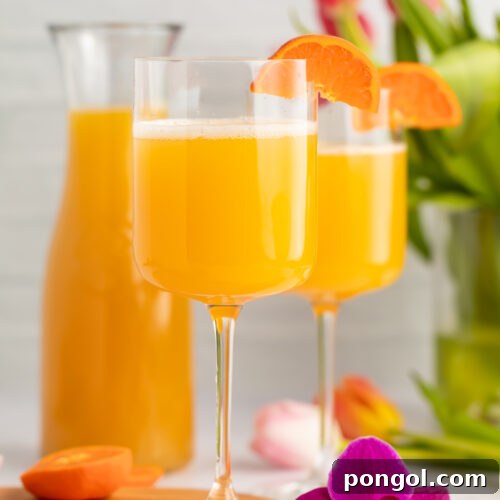 Side view of two wine glasses holding POG juice mimosas with a carafe of pog juice in the background.