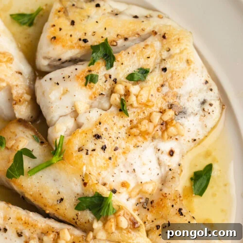 Lemon garlic barramundi in a white bowl with chopped parsley and lemon butter sauce.