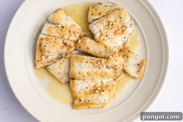 Overhead view of lemon garlic barramundi fillets in a white ceramic bowl.