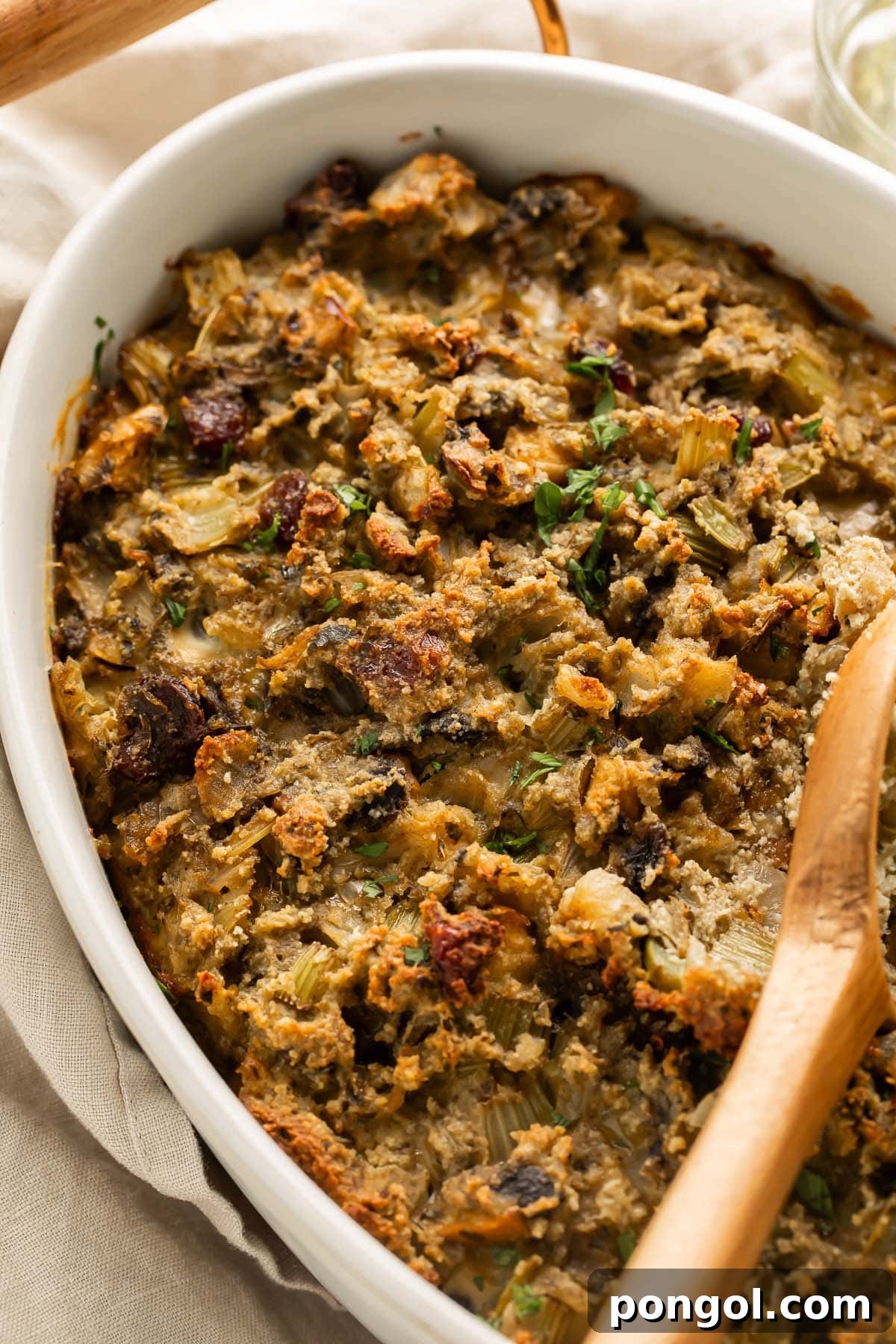 Wholesome Paleo Stuffing Grain Free 3 A wooden spoon rests gently on a mound of golden paleo stuffing in an oval ceramic casserole dish, placed on a rustic holiday table adorned with subtle festive decorations.
