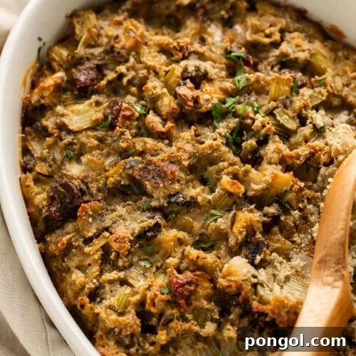 A wooden spoon rests on paleo stuffing in an oval ceramic casserole dish on a holiday table.