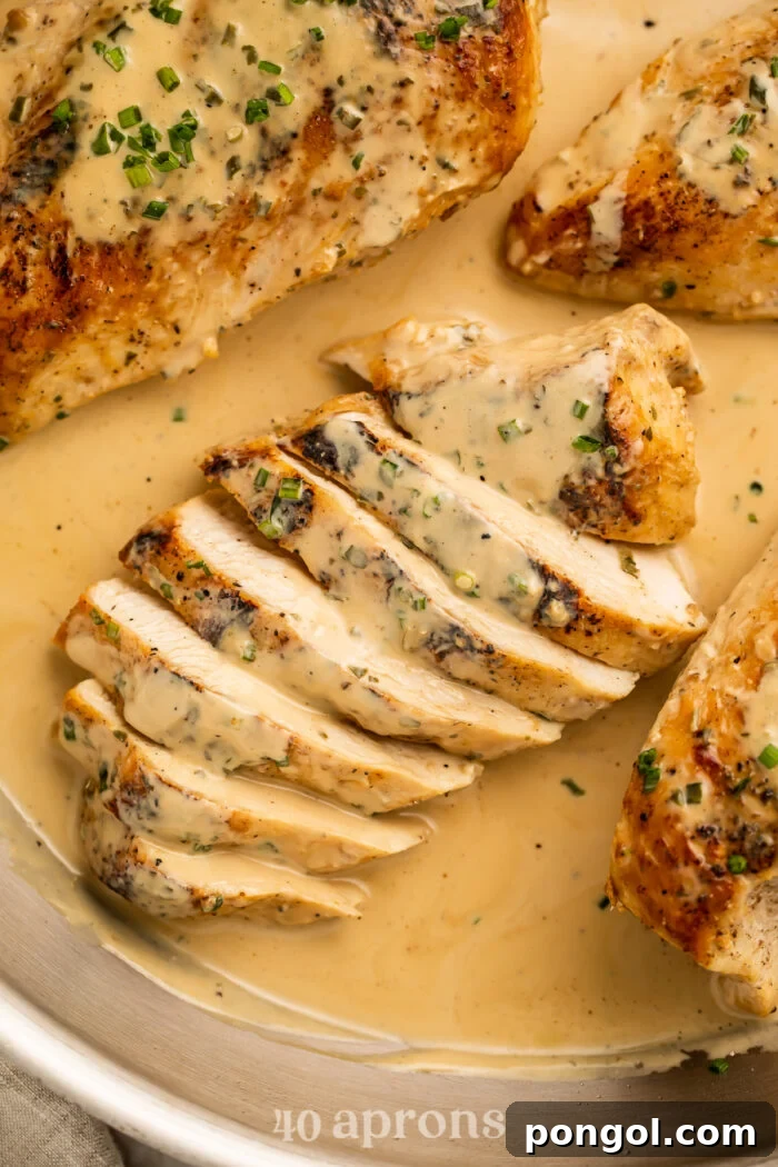 Overhead, close-up view of a sliced chicken breast in a skillet with creamy Boursin sauce and chopped chives.