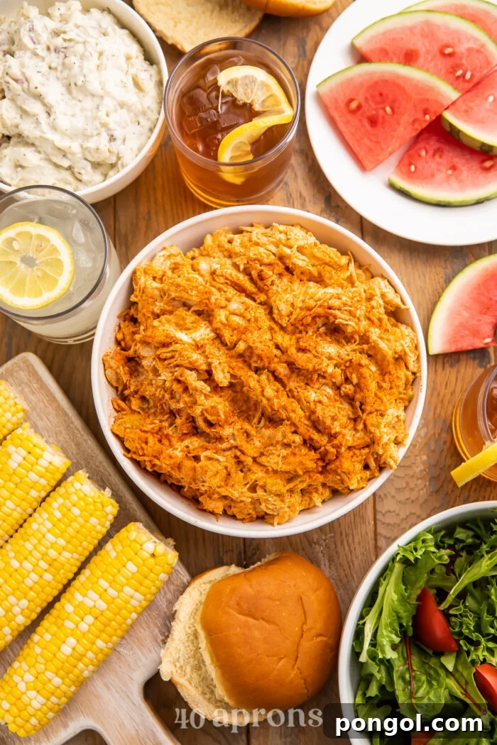 Smoky BBQ Chicken Salad 2 Overhead view of BBQ chicken salad in a bowl surrounded by corn on the cob, watermelon slices, and other barbecue essentials.