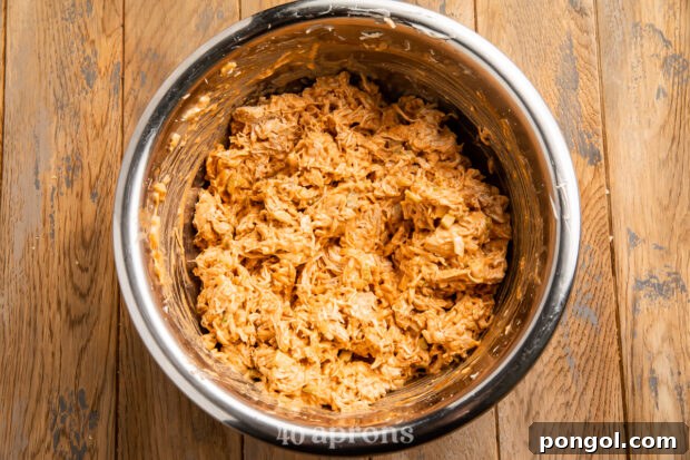 Overhead view of fully mixed BBQ chicken salad in a large silver mixing bowl on a wooden counter.