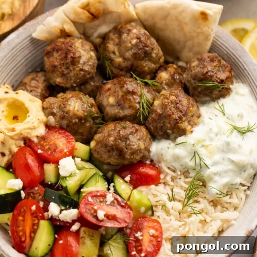 A close-up view of a beautifully arranged Gyro Bowl featuring succulent meatballs, fluffy lemon rice, cooling tzatziki, and a fresh cucumber salsa, served with naan bread.