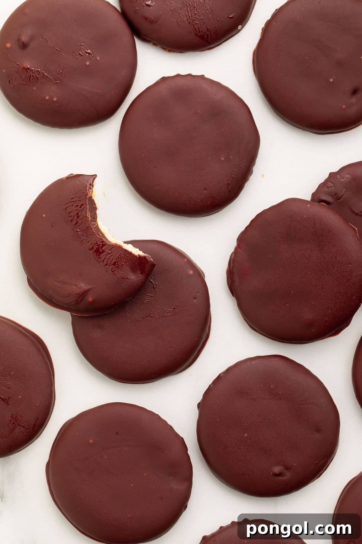 Classic Vegan Chocolate Mint Cookies 3 Vegan thin mints scattered across a countertop. A bite is missing from the topmost cookie.