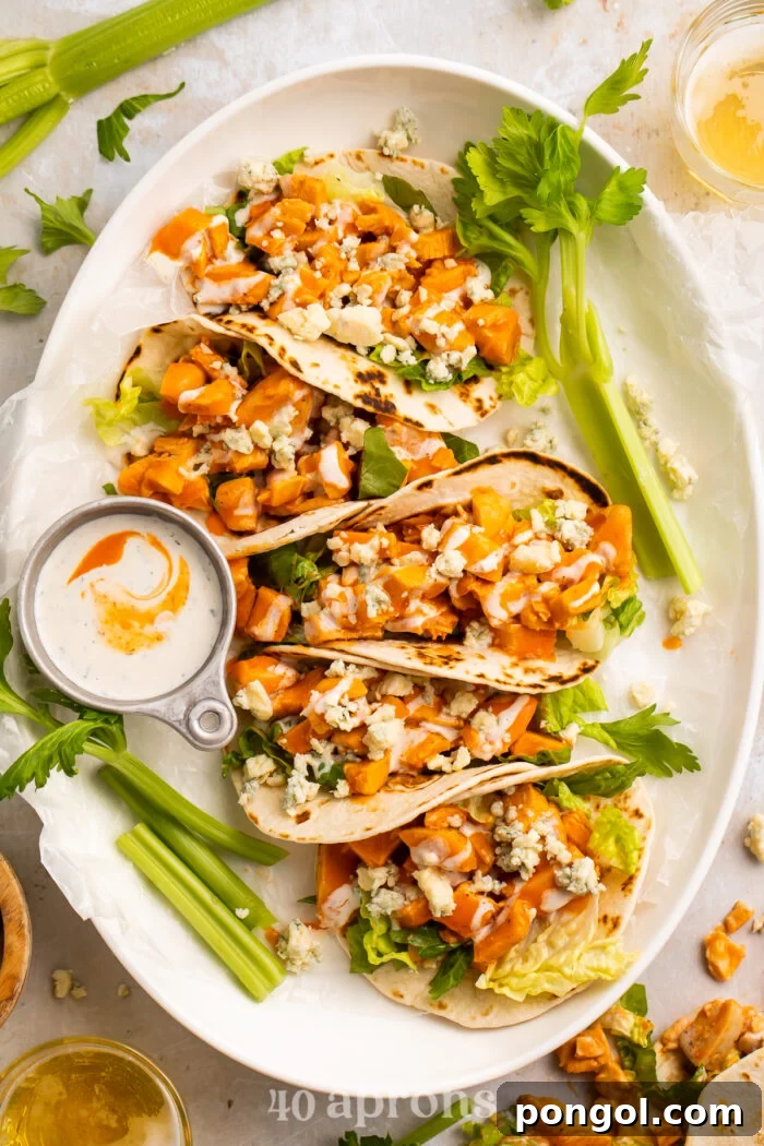 Overhead view of 5 buffalo chicken tacos lined vertically on an oval platter with celery sticks and ranch.