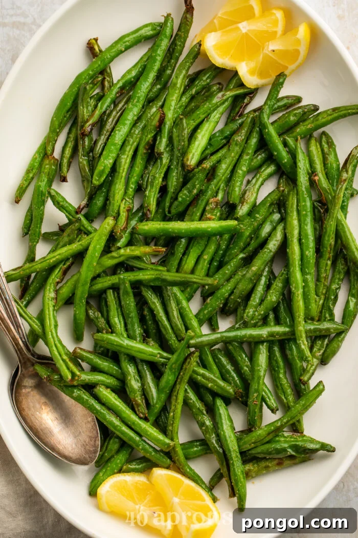 Close-up of air fryer green beans on a white serving platter with lemon wedges and a silver spoon.