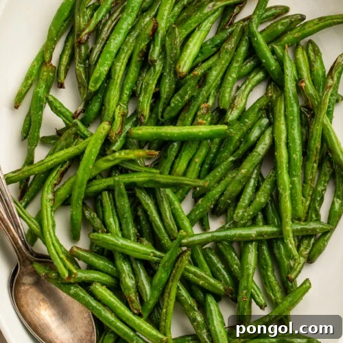 Close-up of air fryer green beans on a white serving platter with lemon wedges and a silver spoon.