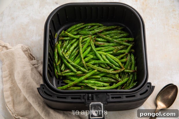 Overhead view of cooked green beans in an air fryer basket on a white counter.
