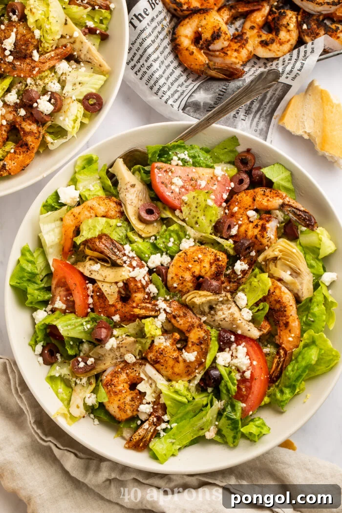 Overhead view of a giant bowl of blackened shrimp salad with feta, kalamata olives, artichoke hearts, and tomatoes, ready to be served.