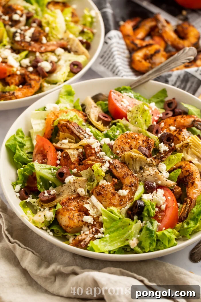3/4-angle view of a blackened shrimp salad, showcasing the fresh lettuce, ripe tomatoes, briny olives, and creamy feta cheese, all topped with perfectly cooked shrimp.