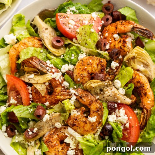 Close-up of blackened shrimp salad with tomatoes, olives, and feta, highlighting the texture and colors.