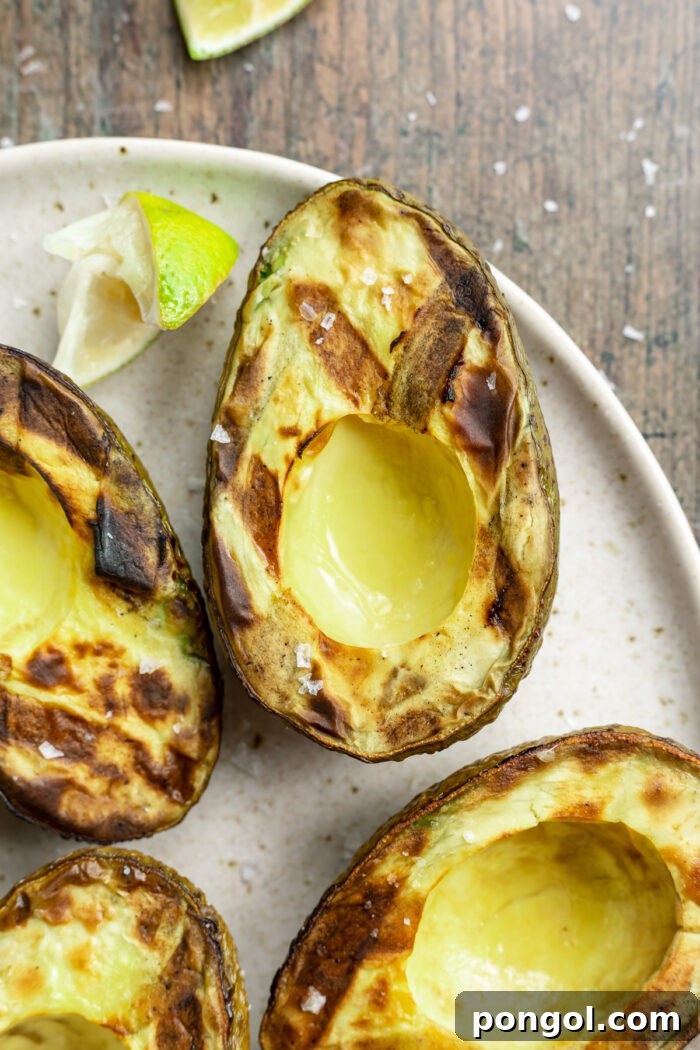 Fire-Kissed Avocado 3 Close-up of a grilled avocado on a plate with lime wedges and other avocados.