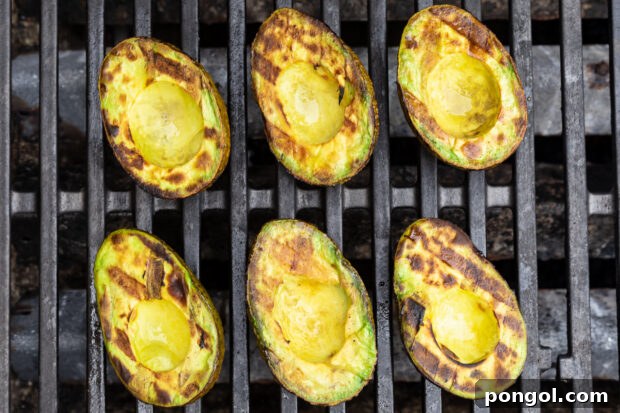 Overhead view of 6 avocado halves on a grill, with char marks criss-crossing on avocado meat.