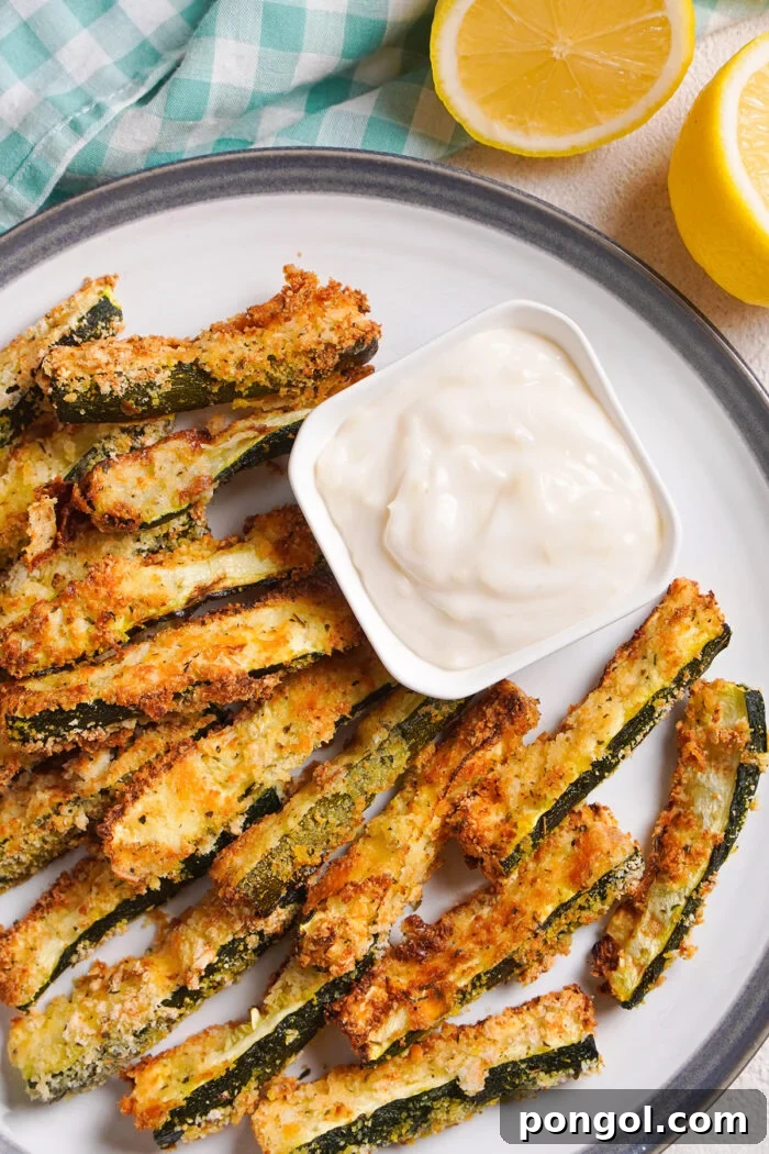 Overhead view of air fryer zucchini fries on a round plate with a square ramekin of garlic aioli.