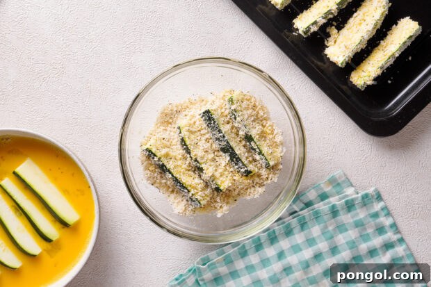 Overhead view of zucchini sticks in glass mixing bowl with breadcrumb mixture.