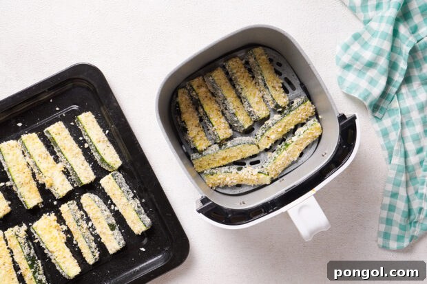 Overhead view of zucchini fries in air fryer basket next to a tray of uncooked zucchini fries.