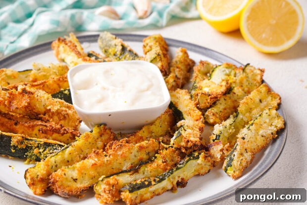 Side view of a platter of air fryer zucchini fries with a ramekin of garlic aioli on a table.