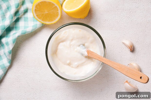 Overhead view of creamy garlic aioli in a small glass mixing bowl with a rubber spatula.