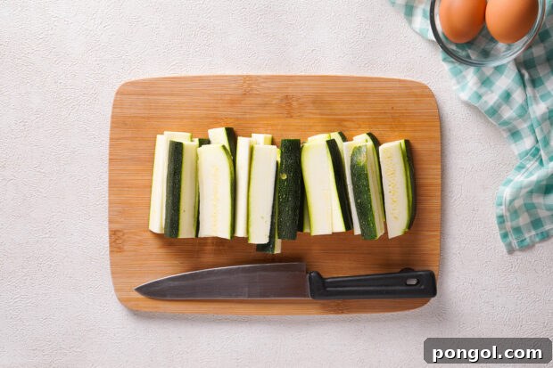 Overhead view of zucchini sticks on a wooden cutting board.