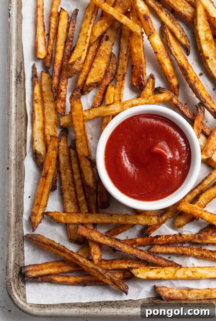 Overhead view of perfectly baked Cajun-seasoned fries on a baking sheet with a ramekin of ketchup, ready to be served.