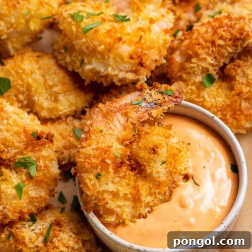 Air fryer shrimp on a neutral plate with a ramekin of sriracha mayo. One shrimp rests in the mayo.