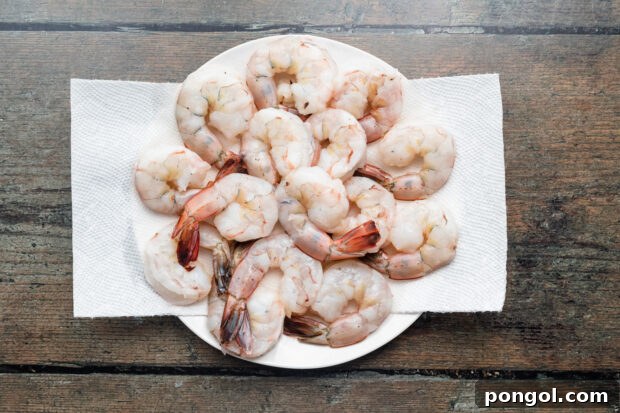 Overhead view of peeled and deveined raw shrimp on a paper towel on a plate.