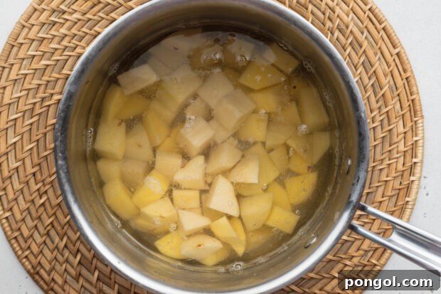Overhead view of cubed potatoes in a saucepan on a neutral background.