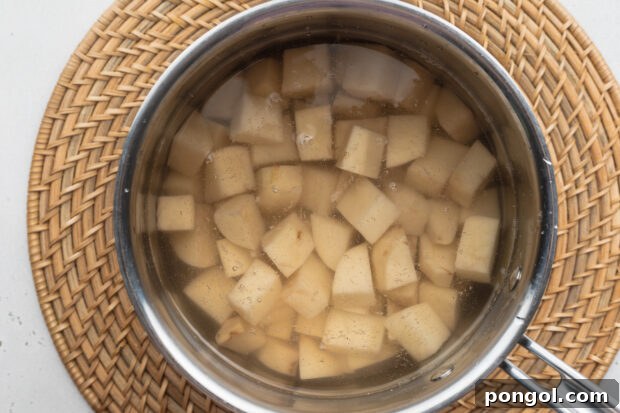 Overhead view of cubed russet potatoes in a saucepan on a neutral background.