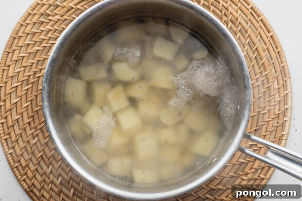 Overhead view of boiled, cubed russet potatoes in a saucepan on a neutral background.