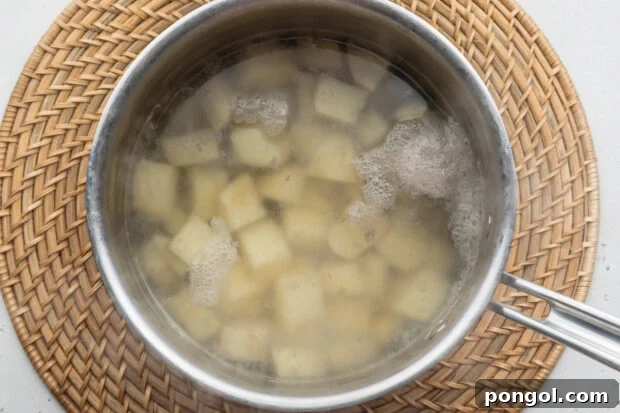 Overhead view of boiled, cubed russet potatoes in a saucepan on a neutral background.