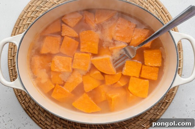 Overhead view of boiling, peeled, cubed sweet potatoes in a large pot.