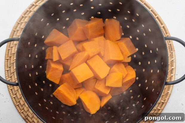 Overhead view of boiled sweet potato cubes in a large black colander/