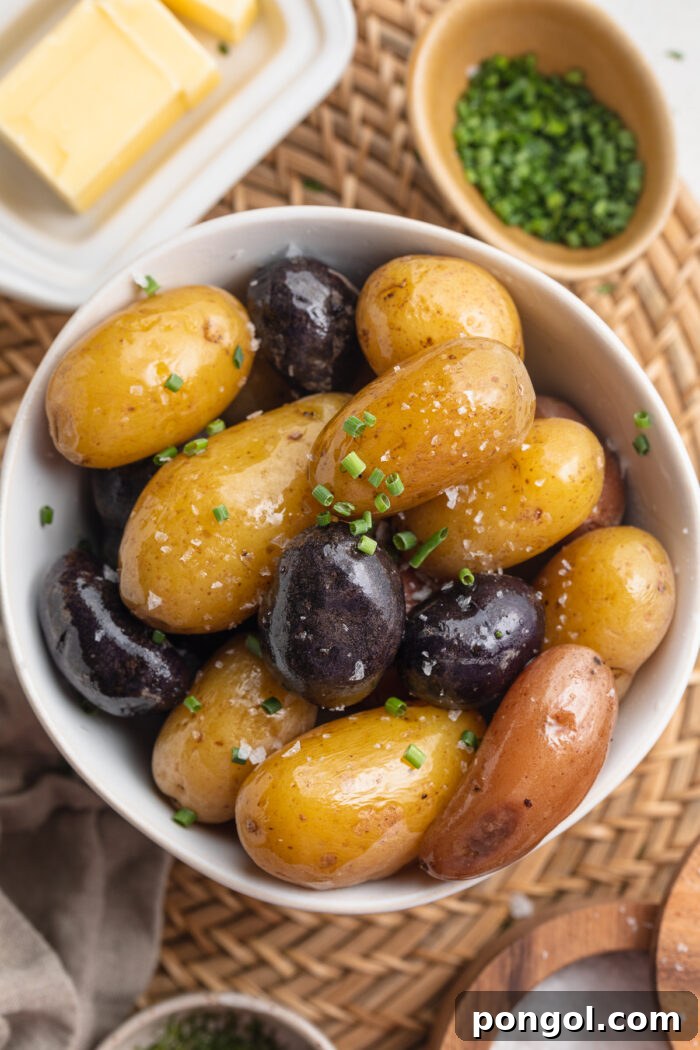 Overhead view of boiled light and dark potatoes in a white bowl on a wooden table surrounded by potato toppings.