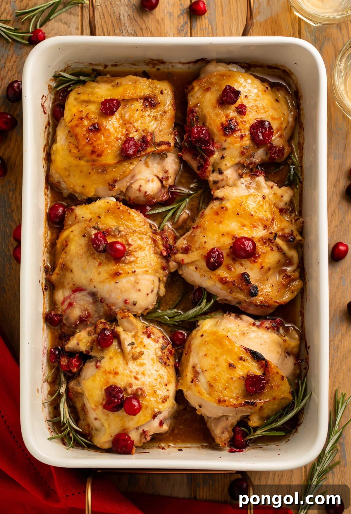 Easy One-Pan Cranberry Rosemary Chicken 3 Overhead view of six roasted chicken thighs with cranberries and rosemary in white baking dish, ready to serve.