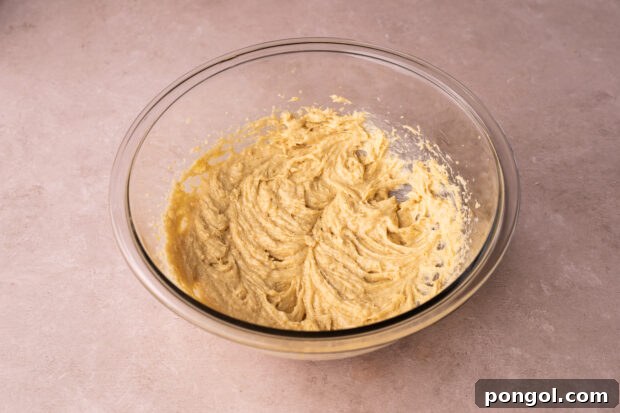 Effortless Air Fryer Chocolate Chip Cookies 5 Side-angle view of butter, white sugar, and brown sugar creamed in a large glass mixing bowl on a pink surface.