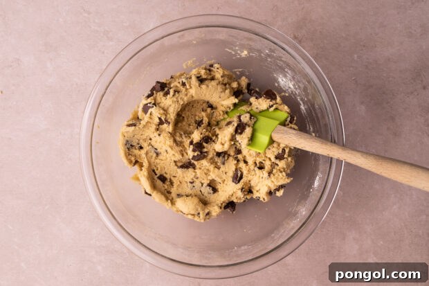 Effortless Air Fryer Chocolate Chip Cookies 7 Overhead view of chocolate chip cookie dough in a large glass mixing bowl with a silicone spatula.